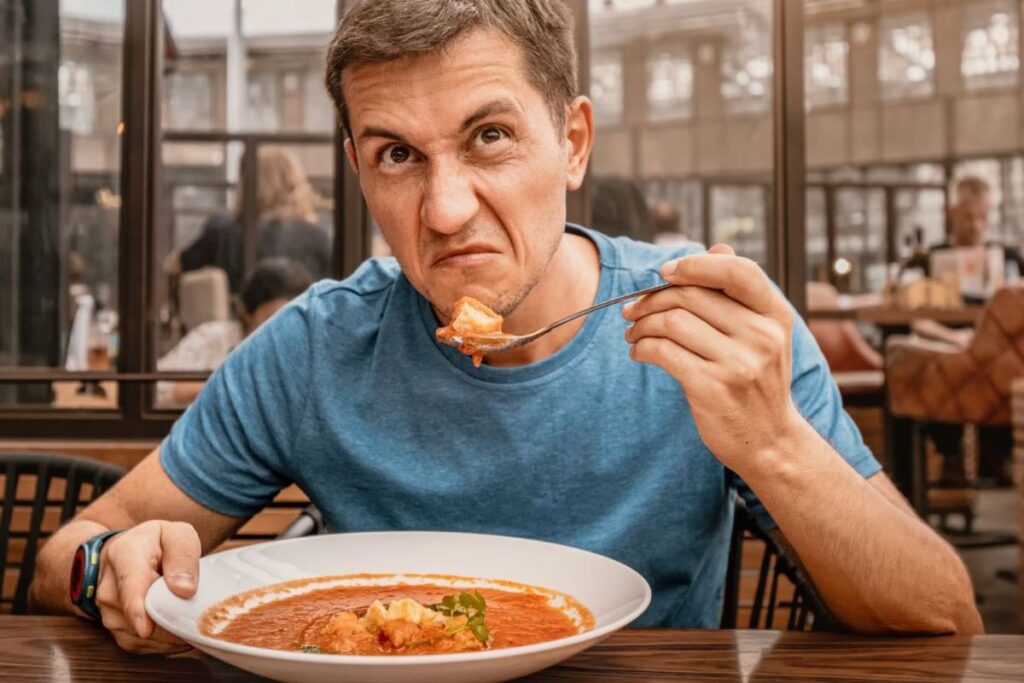 Man eating a plate of pasta looking annoyed 