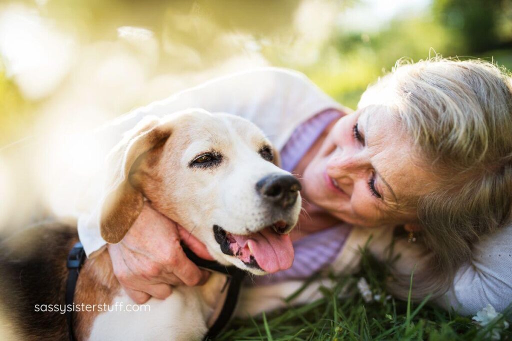 a middle aged woman and her dog lay in the grass happily together.