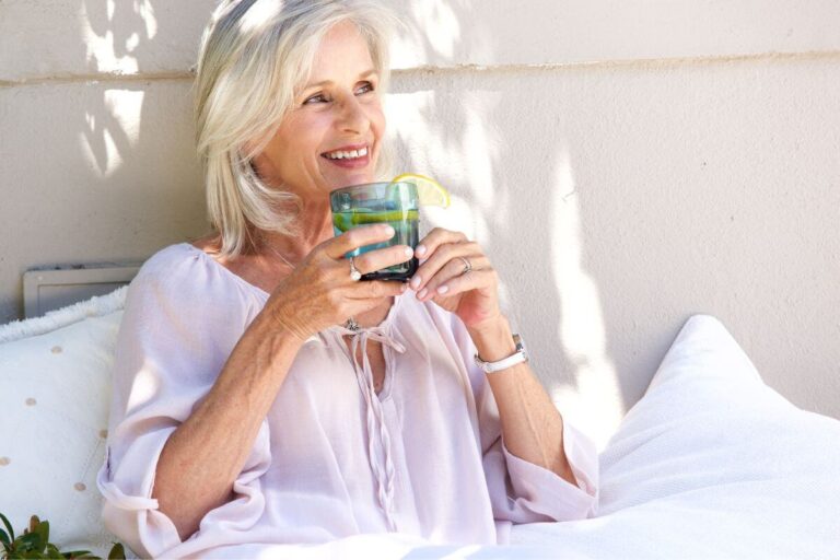 middle aged woman drinking a glass of water with lemon in is as she relaxes.