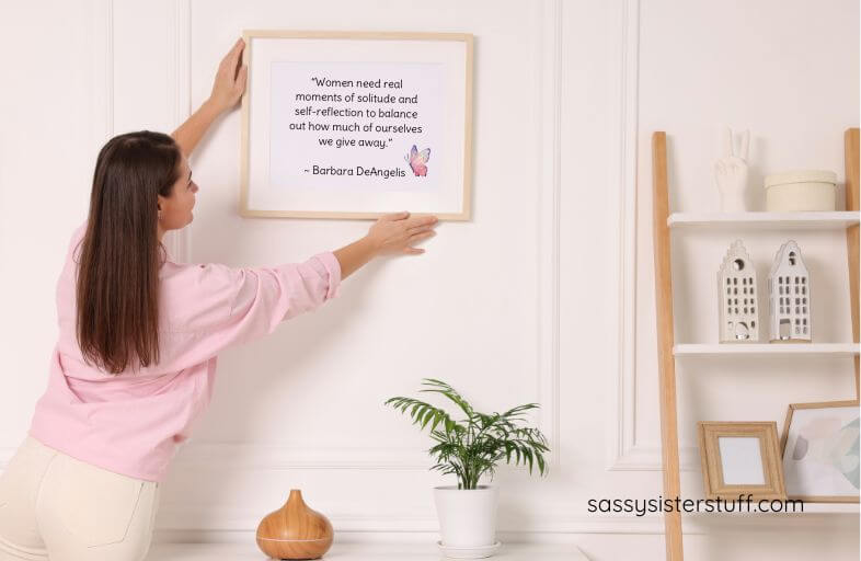 a woman hangs wall art on above an essential oil diffuser and a plant.