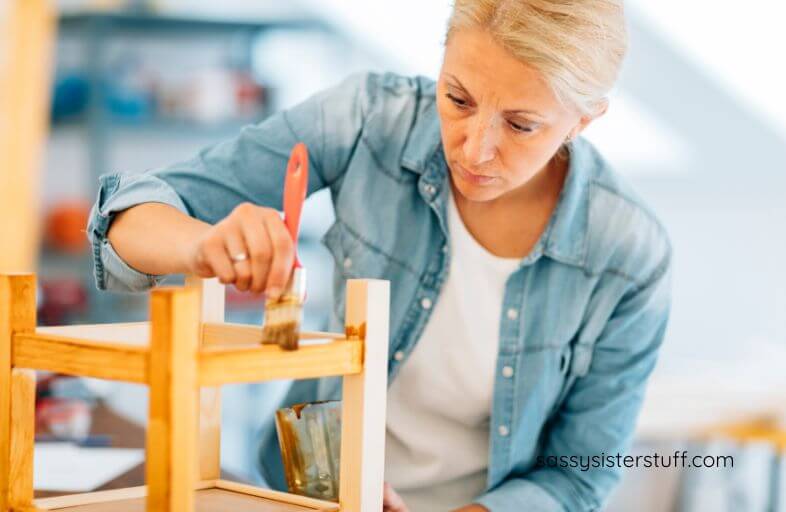 a middle aged woman paints the bottom of a chair to refresh her living space.