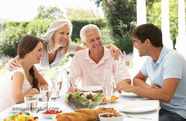 middle aged mother and father, adult son, and adult daughter enjoy lunch together on the patio.