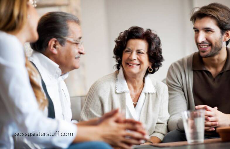 middle age mother and father with adult son and adult daughter sit together chatting.