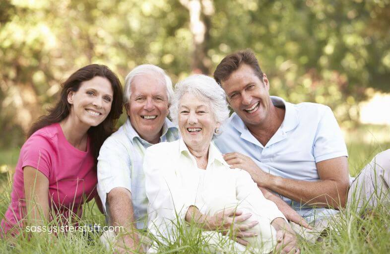 middle age mother and father, adult son, and adult daughter pose for a photo on the grass in a park.