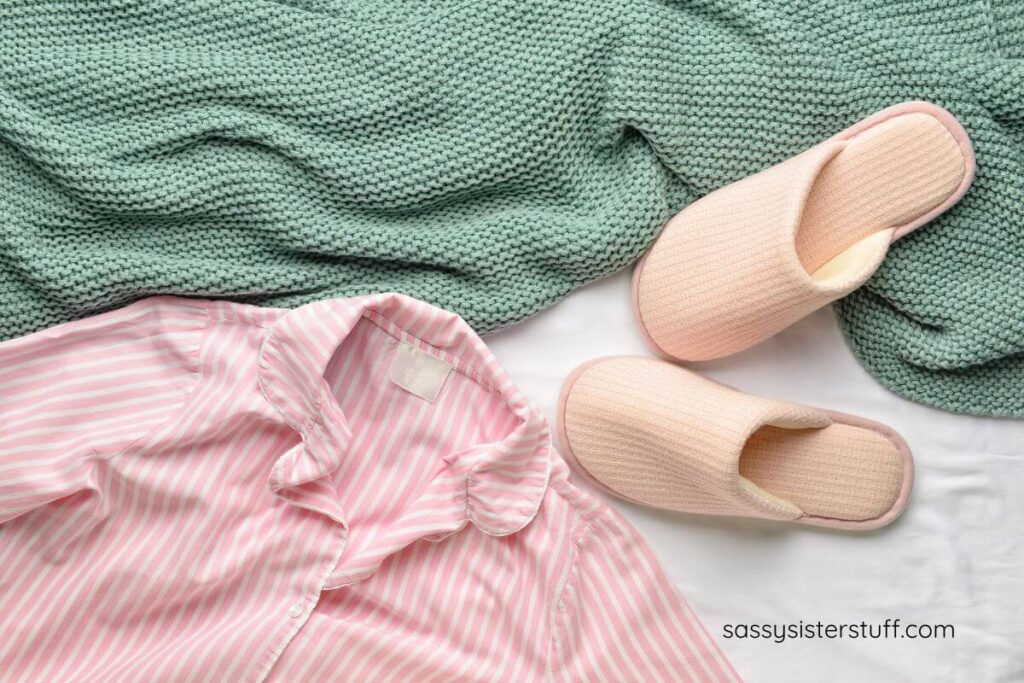 flat lay of a cozy blanket, slippers, and pajamas on a bed with white sheets.