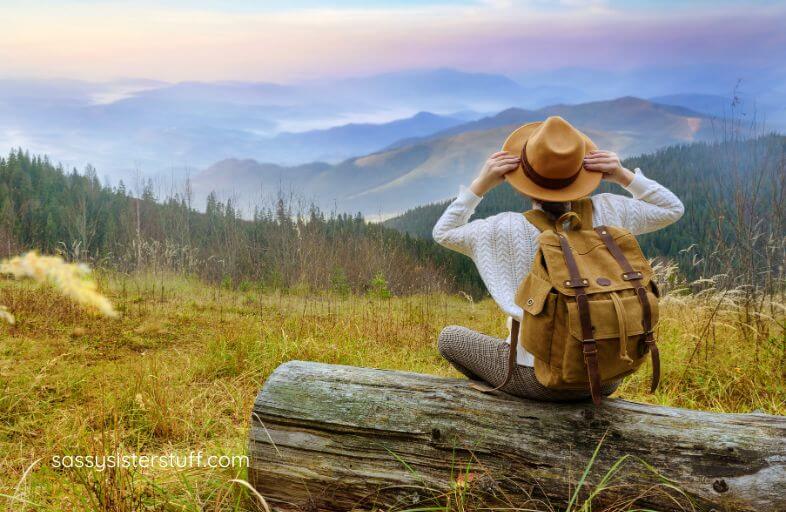 a woman sits on a large log overlooking mountains off in the distance.