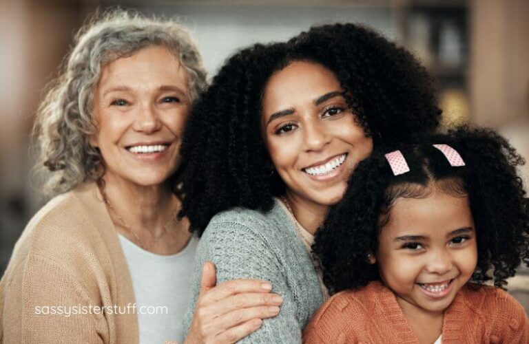 middle aged mom, adult daughter, and granddaughter pose for a happy picture together