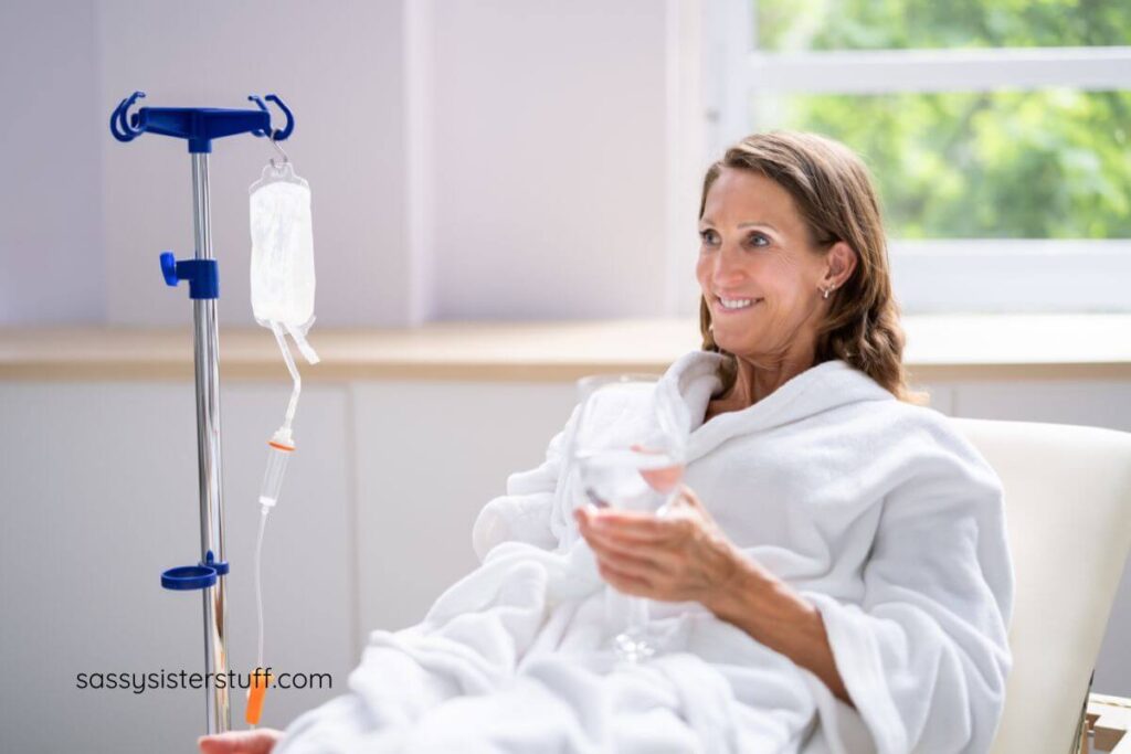 middle aged woman relaxes with a glass of water while she gets an IV drip.