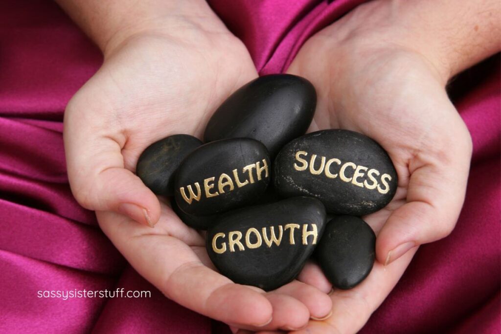 close up of two hands holding black rocks that say wealth, success, and growth.