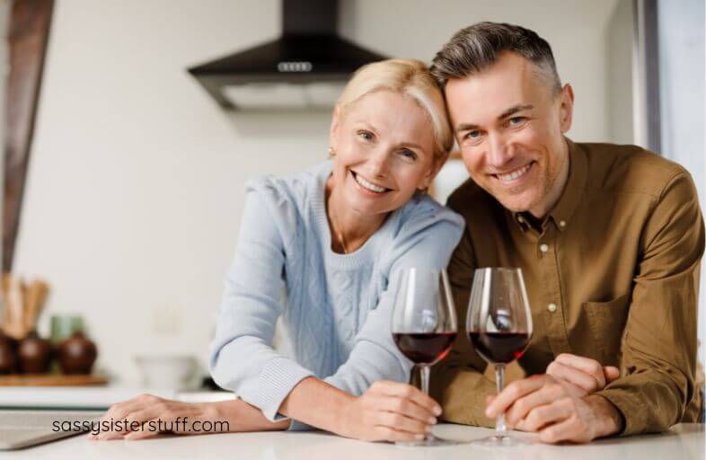 middle aged couple happily pose for a photo with two glasses of red wine