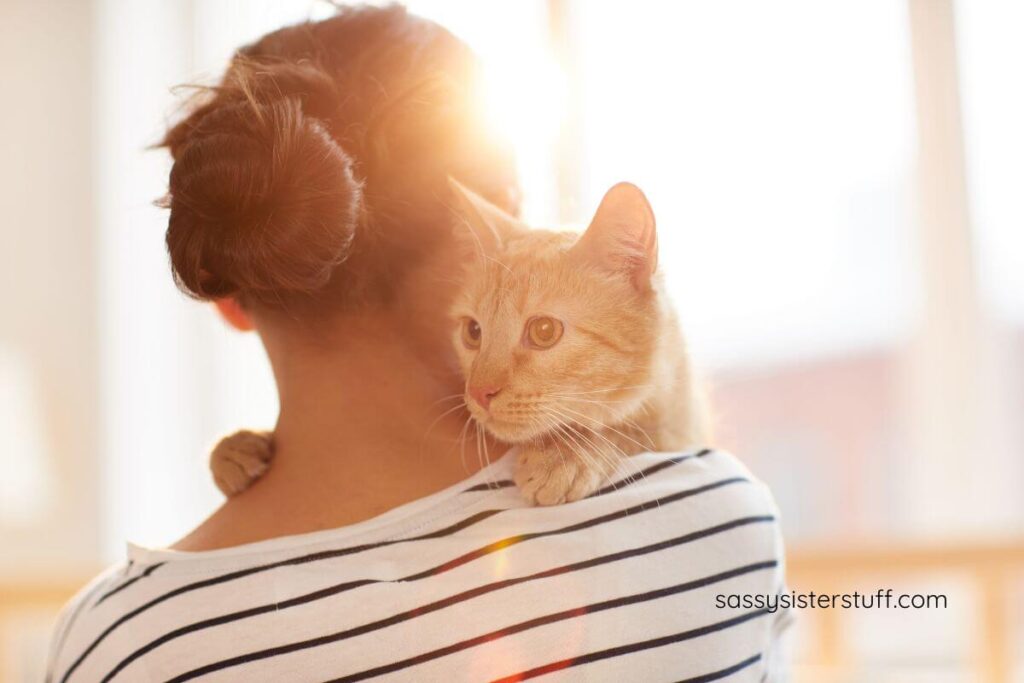 woman holding a cat who is peeking over her shoulder.