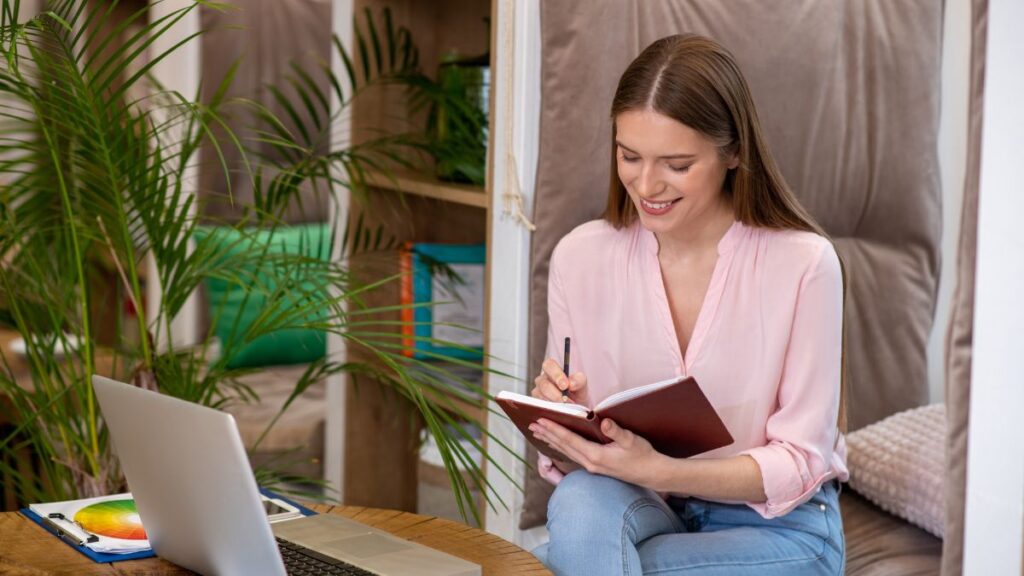 woman writing in journal with computer