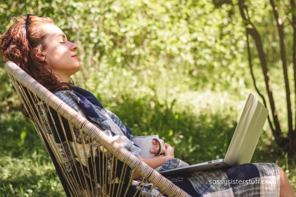 woman sitting outside getting some sun taking a break from work, relaxing with her eyes closes and her laptop in her lap.