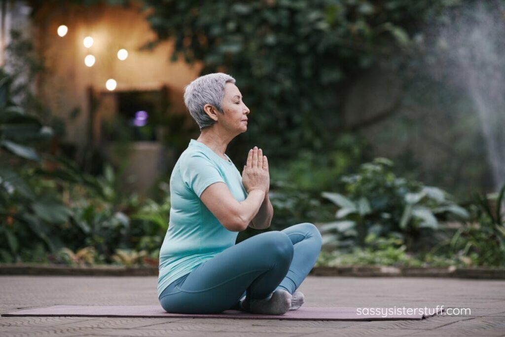 middle aged woman sitting outside on a mat doing yoga.