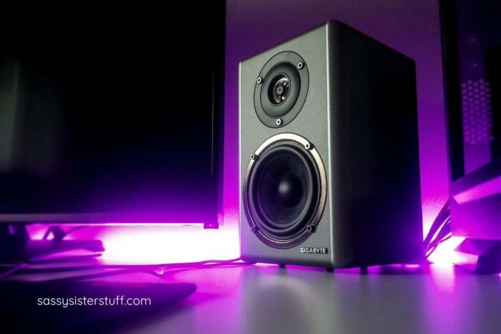 Large speaker sitting on the floor with purple party lights around it.