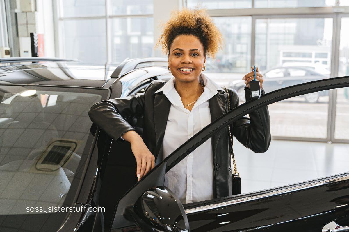 a very proud female stands next to her new car in a dealership.