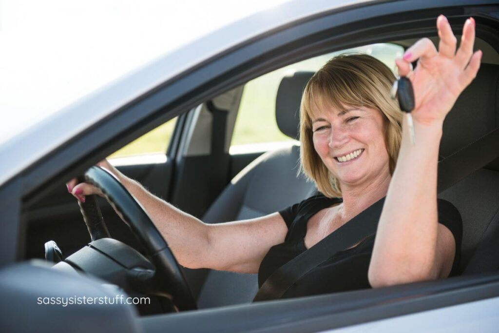 a woman sits in the drivers seat of a new vehicle she just bought and shows the keys.