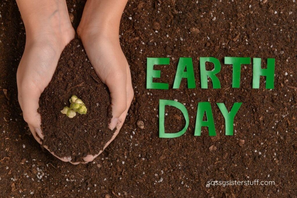 hands scooping up a buddling plant in the soil and letters that say Earth Day.