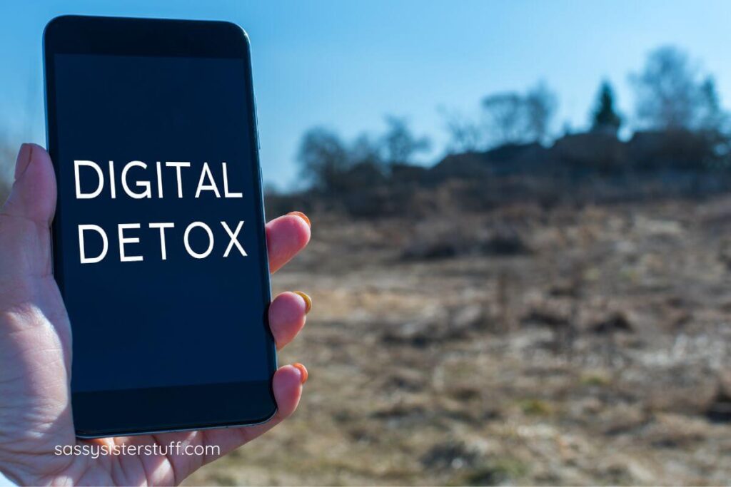 female hand holds a mobile phone that says digital detox on it.