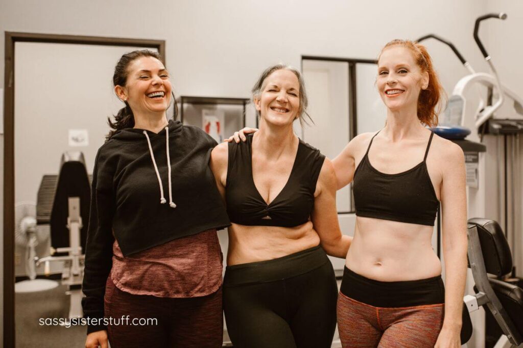 three happy middle aged women in exercise clothing pose for a photo.