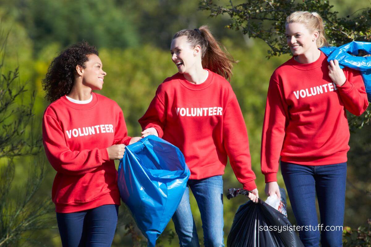 three females in red volunteer sweatshirts clean up a park for Earth Day.