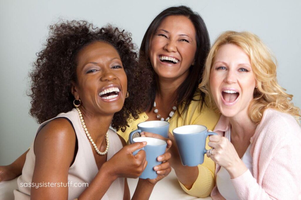 three cheerful middle aged ladies laughing together over a cup of coffee.