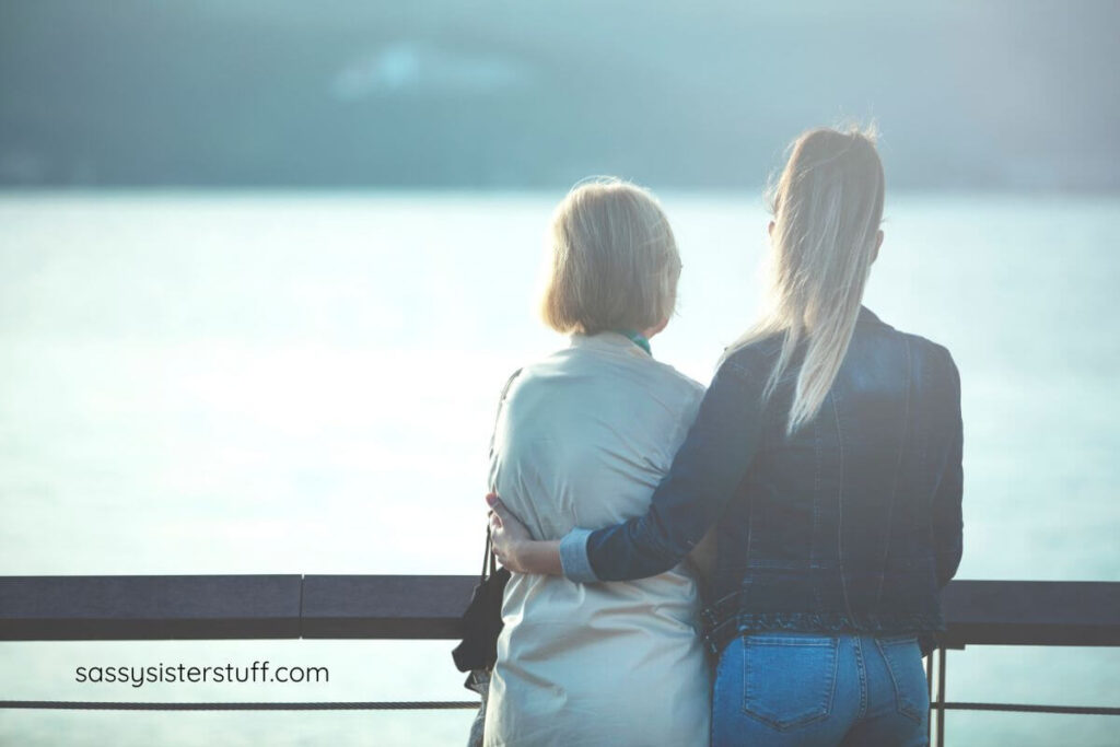 adult woman and her aging mother with dementia stop on the boardwalk and look out over the water.