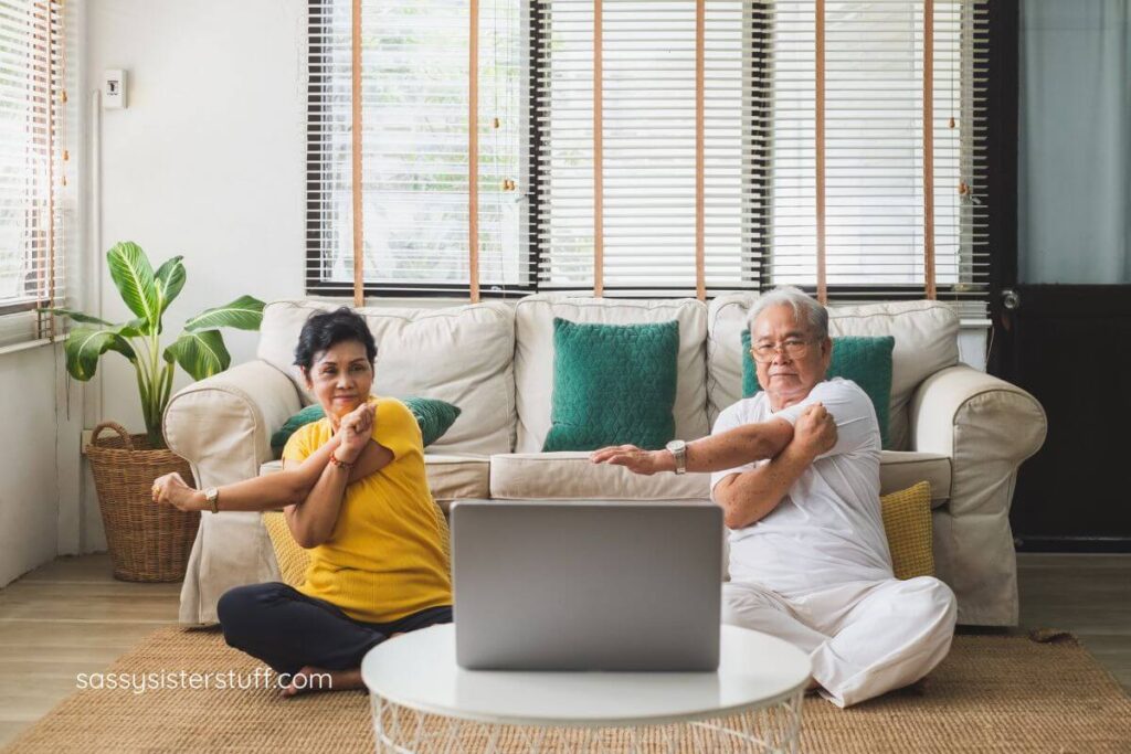 elderly couple sitting on the floor following a YouTube tutorial for low impact stretches.