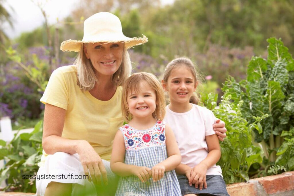 a grandmother and young two granddaughters take a photo in a garden.