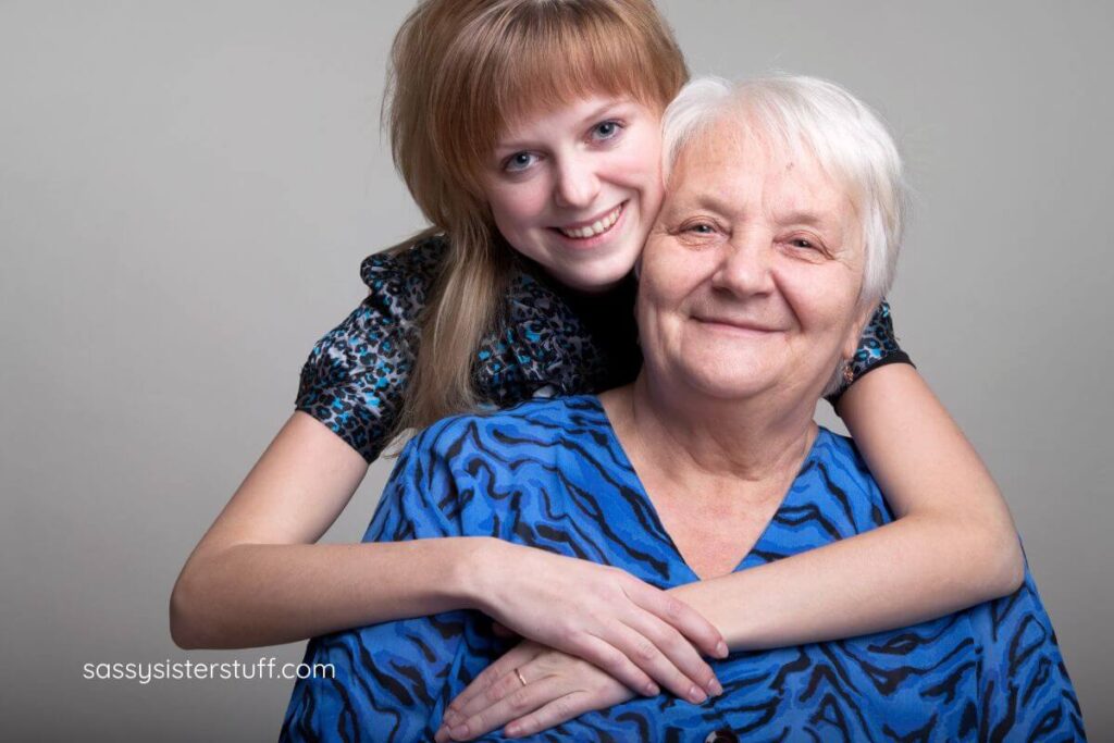 adult granddaughter embraces her grandmother from behind for a picture.