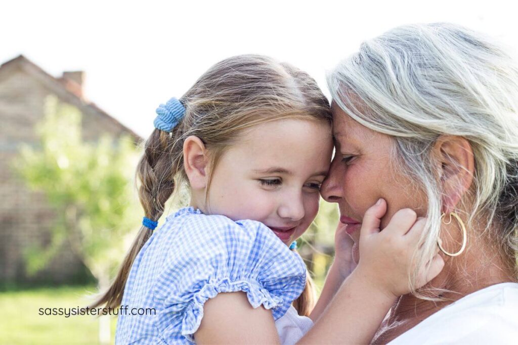 young granddaughter pinches her grandmothers cheeks affectionately as the rest their foreheads against each other.