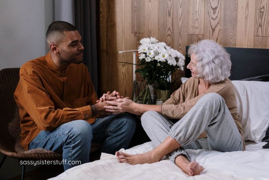 grandmother and adult grandson hold hands and smile at each other.