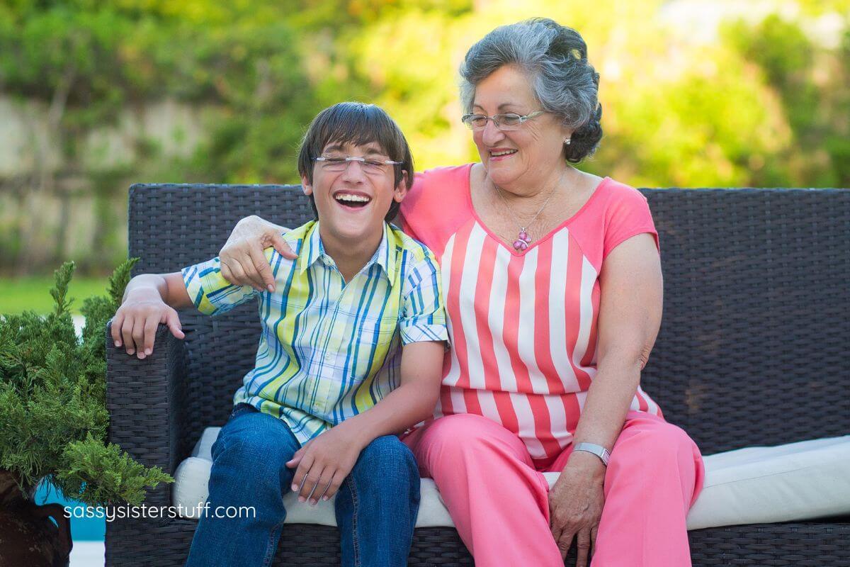 grandmother and young grandson sit on an outdoor sofa laughing together.