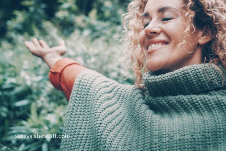 close up of middle aged women in nature, with her eyes closes, smiling, and with her arm stretched out.