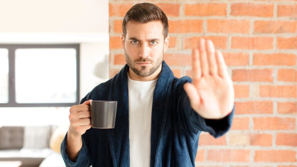 man showing stop with hand holding coffee