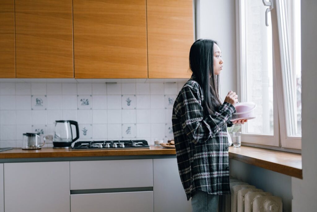 A Woman Eating while Looking Outside a Window
