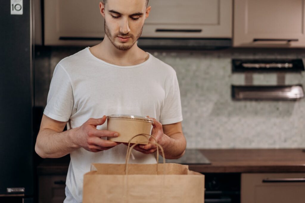 Man in White Shirt Holding Brown Paper Container